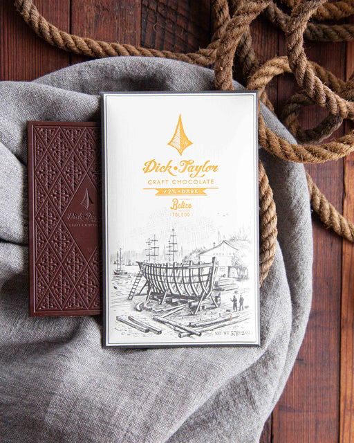 Belize, Toledo Dark Chocolate Bar on top of an unwrapped bar on a blue cloth and wood background with rope as decoration.