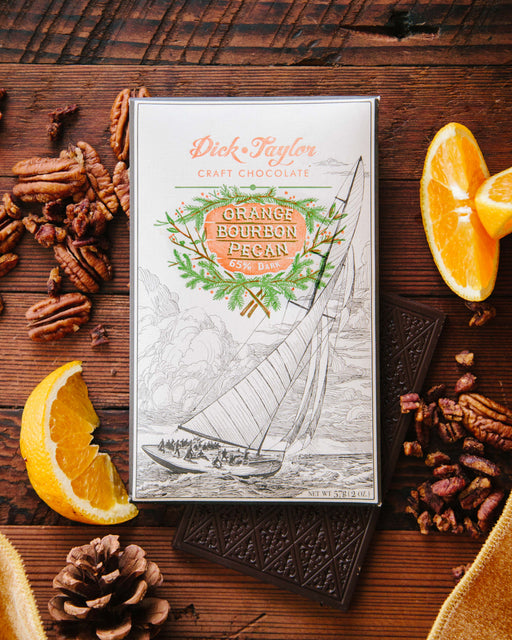 Orange Bourbon Pecan bar on top of an unwrapped bar on a wood background with decorated with orange slices and pecans as decorations.